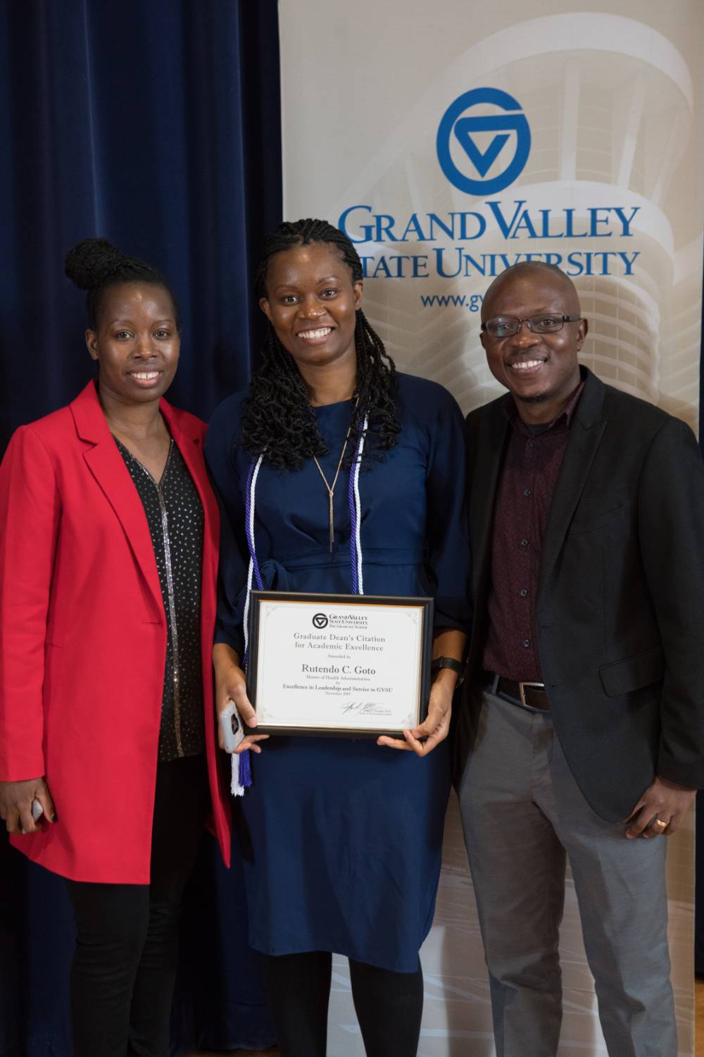Graduate student holding her award with her parents on either side of her